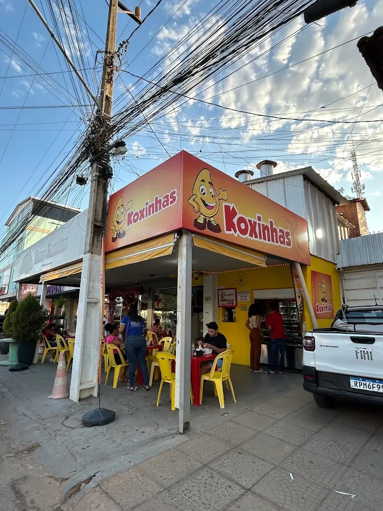 Fachada da Koxinhas com letreiro laranja e mesas do lado de fora